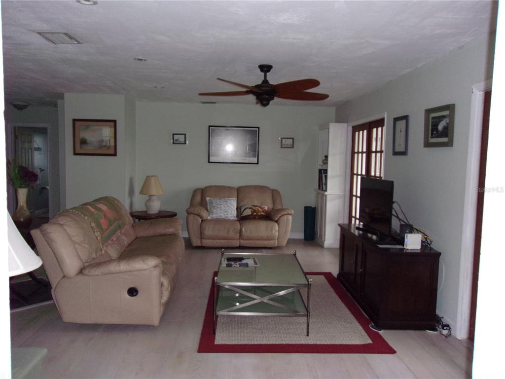 A living room with light wood floors, two tan sofas, a glass coffee table, and ceiling fan — 24279 YACHT CLUB BOULEVARD, PUNTA GORDA, FL