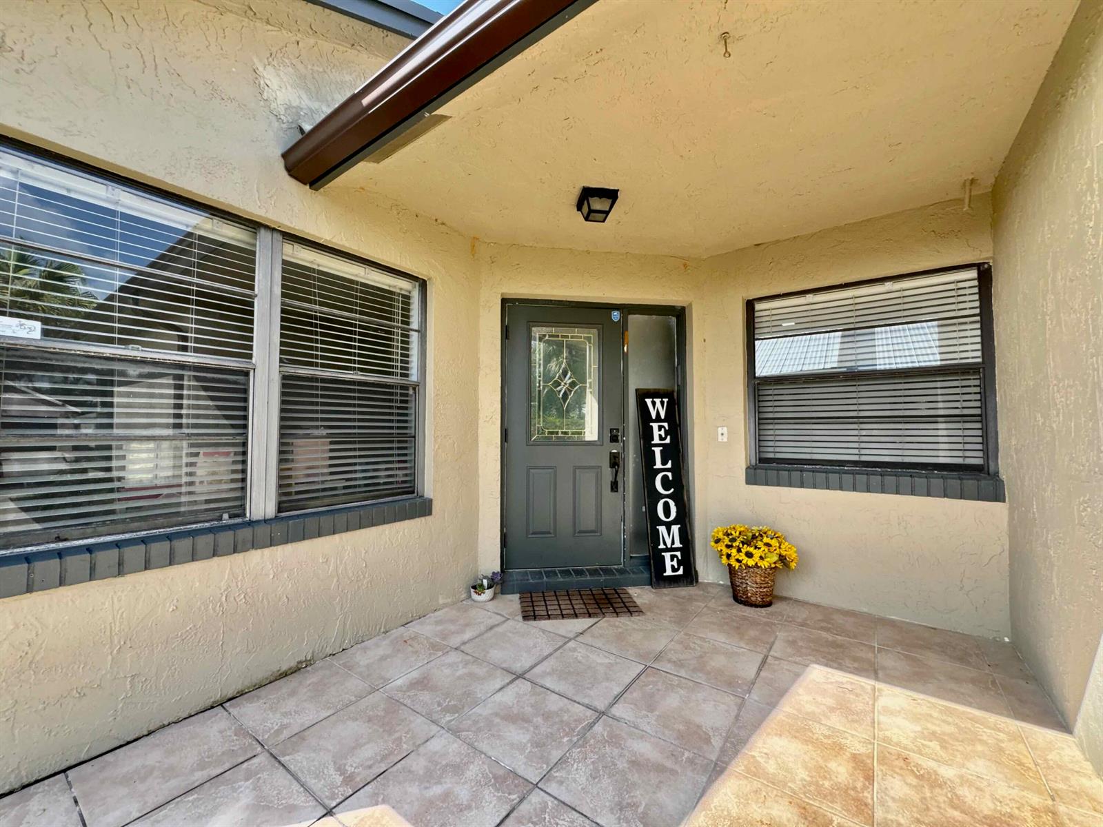 A covered front porch features a dark gray door, tiled flooring, and two windows — 9106 Chatsworth Cascades, Boca Raton FL 33434, BOCA RATON, FL