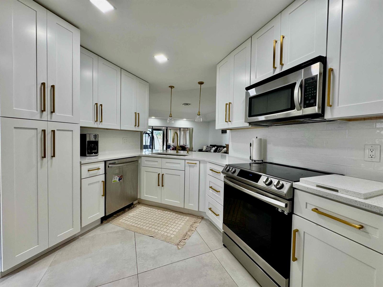 A modern kitchen features white shaker cabinets, gold hardware, stainless steel appliances, and tile flooring — 9106 Chatsworth Cascades, Boca Raton FL 33434, BOCA RATON, FL