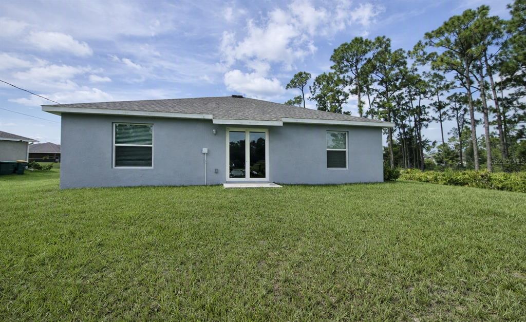 The back exterior of a gray house features a lawn, sliding glass doors, and windows — 23234 ALASKA AVENUE, PORT CHARLOTTE, FL