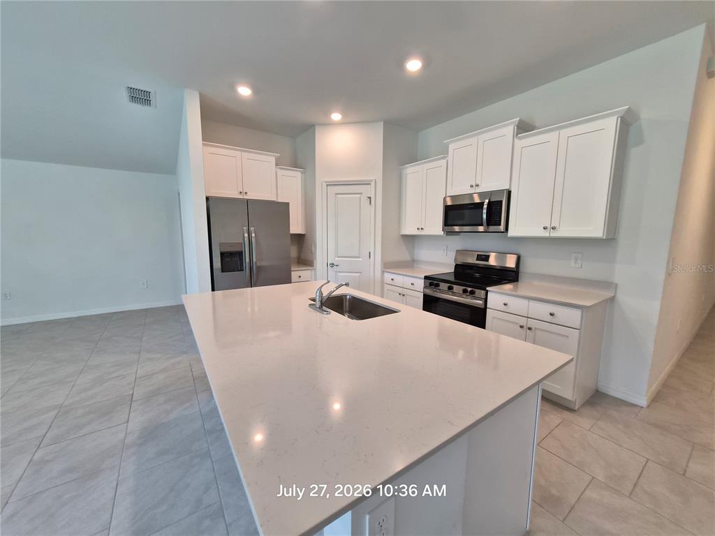 A kitchen features white cabinets, stainless steel appliances, a large island, and light tile flooring — 23234 ALASKA AVENUE, PORT CHARLOTTE, FL