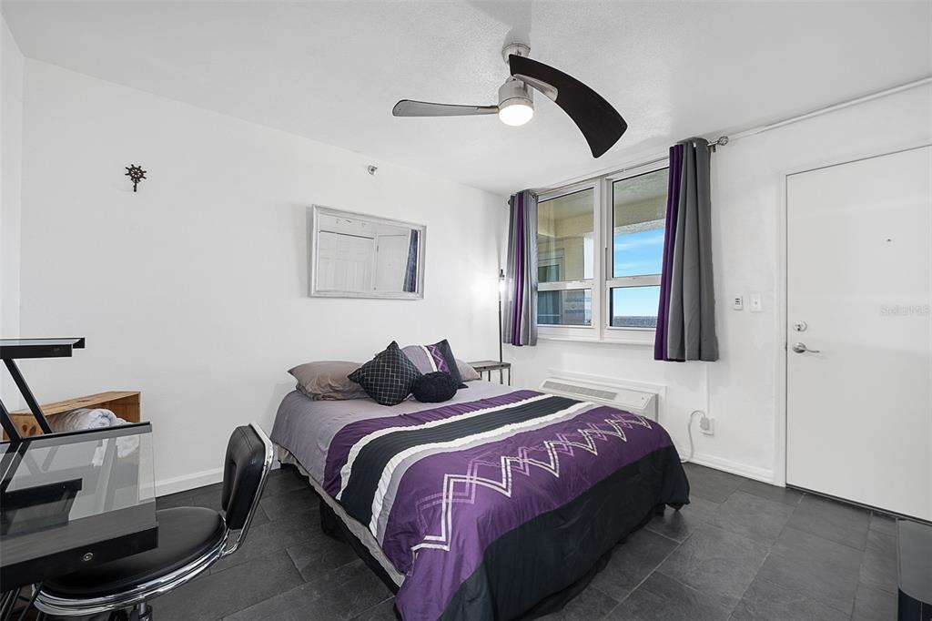 A bedroom features a bed with purple bedding, a ceiling fan, and dark tile flooring — 701 S ATLANTIC AVENUE UNIT 516, DAYTONA BEACH, FL