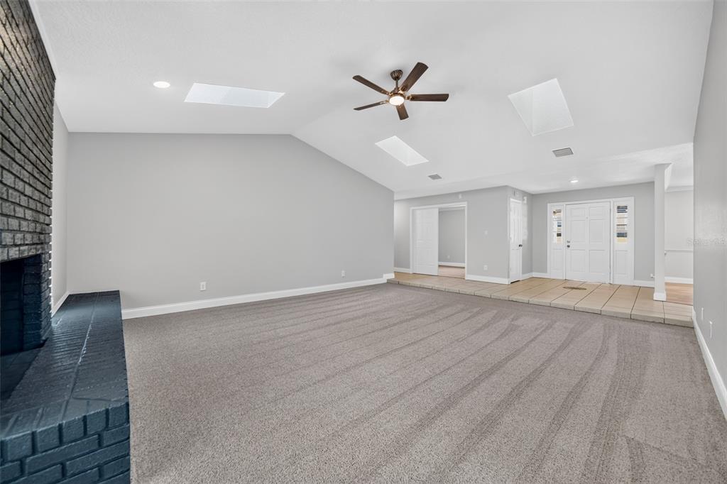 A living room features gray carpet, a black brick fireplace, and a vaulted ceiling — 1390 COR JESU COURT, LONGWOOD, FL