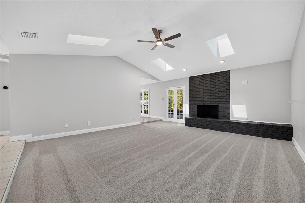 A spacious living room features gray carpeting, a vaulted ceiling with skylights, and a black fireplace — 1390 COR JESU COURT, LONGWOOD, FL