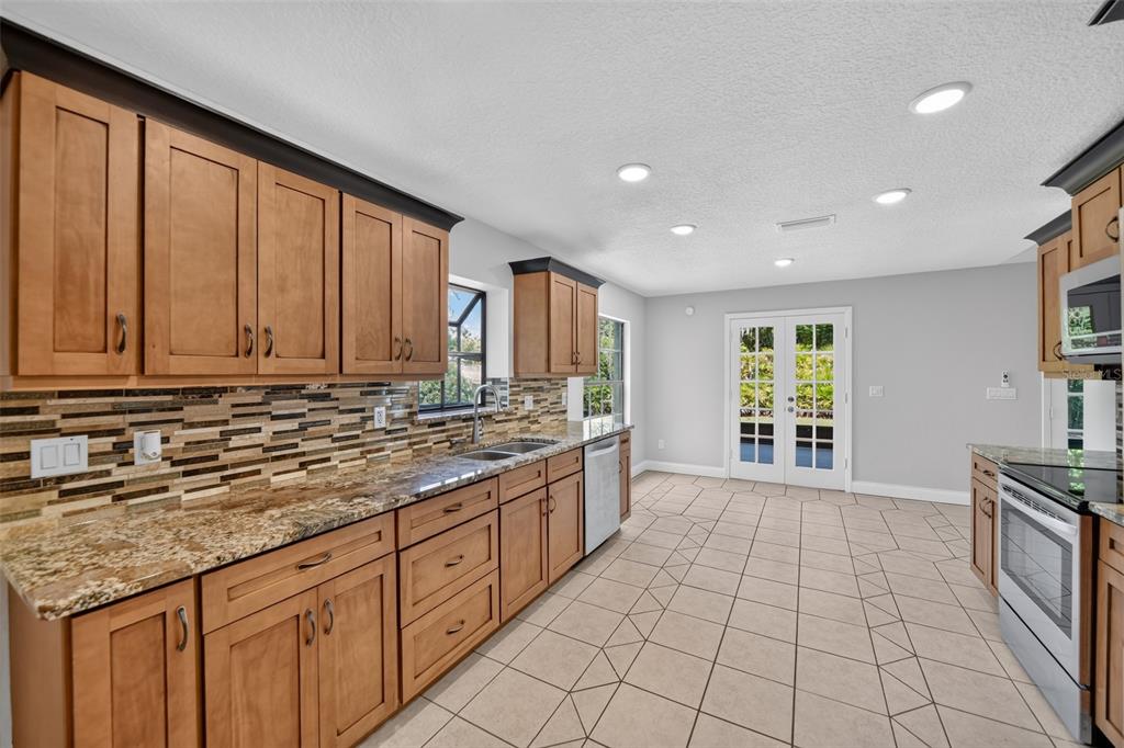 A kitchen with wood cabinets, granite countertops, a tiled backsplash, and light-colored floor tiles — 1390 COR JESU COURT, LONGWOOD, FL