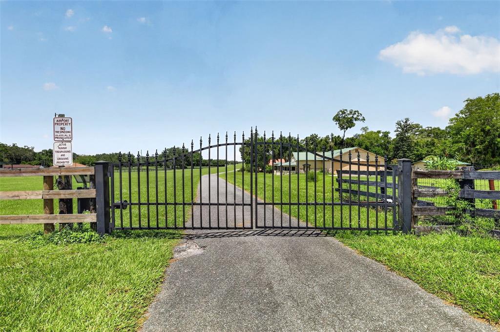 A black metal gate stands at the entrance of a paved driveway leading to a house — 8650 SW 27TH AVENUE, OCALA, FL