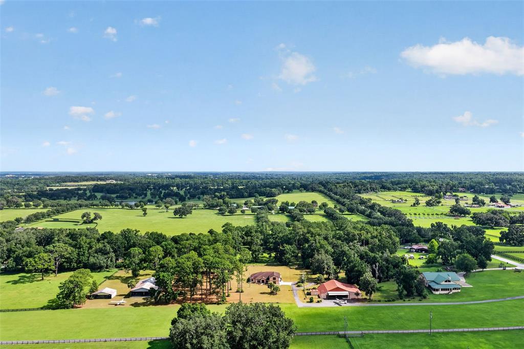 An aerial view shows a rural landscape with several houses, barns, and open green pastures — 8650 SW 27TH AVENUE, OCALA, FL