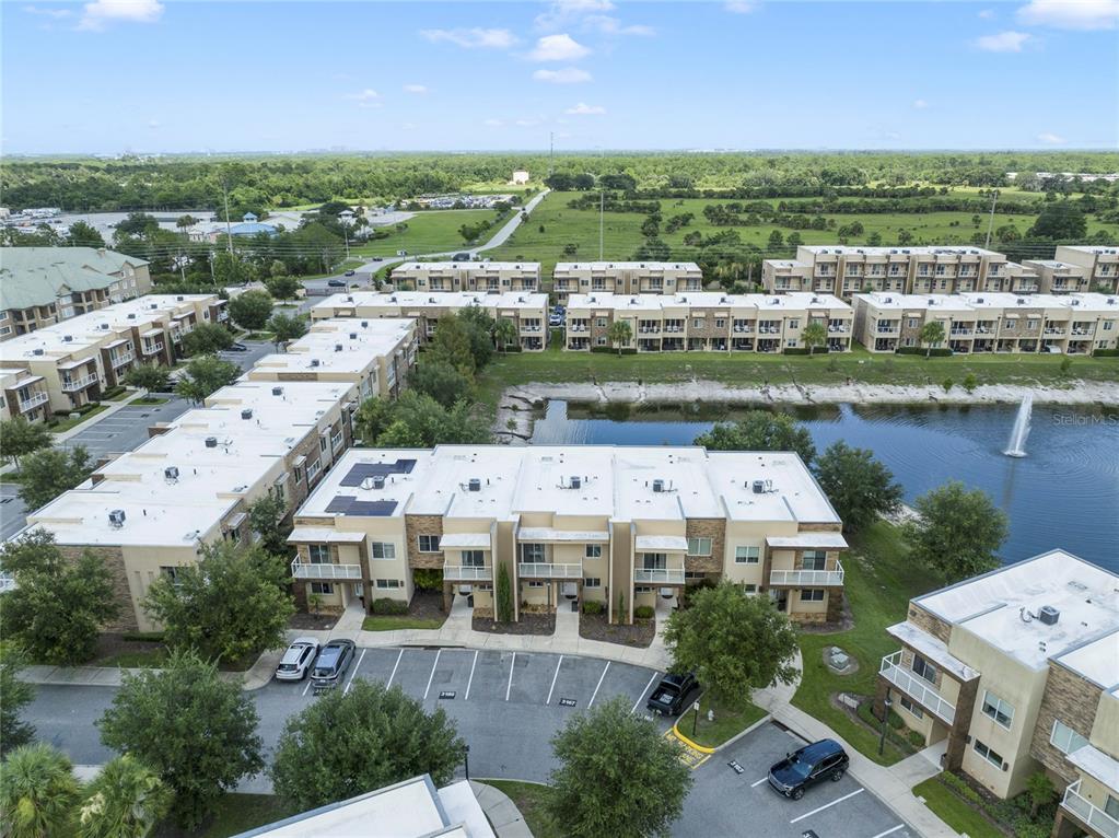An aerial view shows multiple multi-story apartment buildings surrounding a small pond with a fountain — 3169 PANTANAL LANE, KISSIMMEE, FL