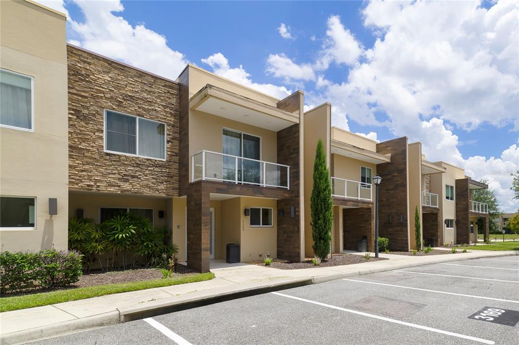 A row of modern townhomes features stone and wood-look siding, balconies, and a paved parking lot — 3169 PANTANAL LANE, KISSIMMEE, FL
