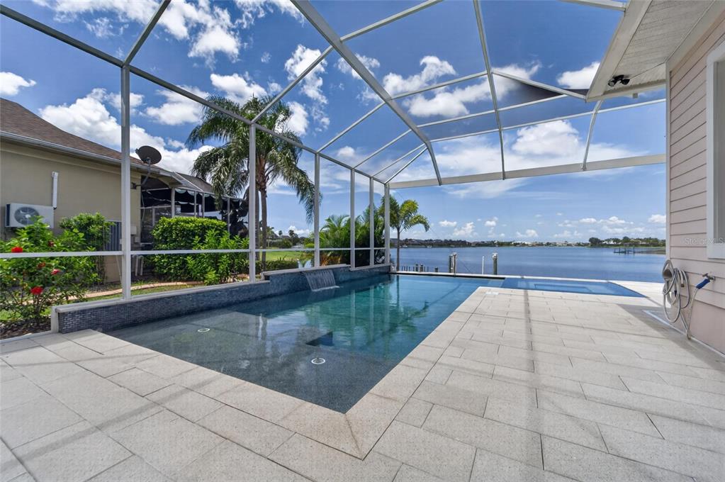 A screened-in pool patio overlooks a lake with a waterfall feature and stone pavers — 429 MANNS HARBOR DRIVE, APOLLO BEACH, FL