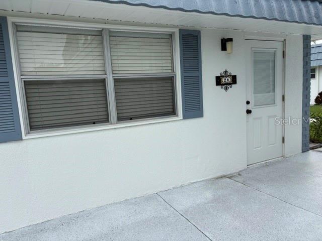 A white exterior wall features a window with blue shutters and a white entry door — 1901 ANDOVER WAY UNIT 26, SUN CITY CENTER, FL