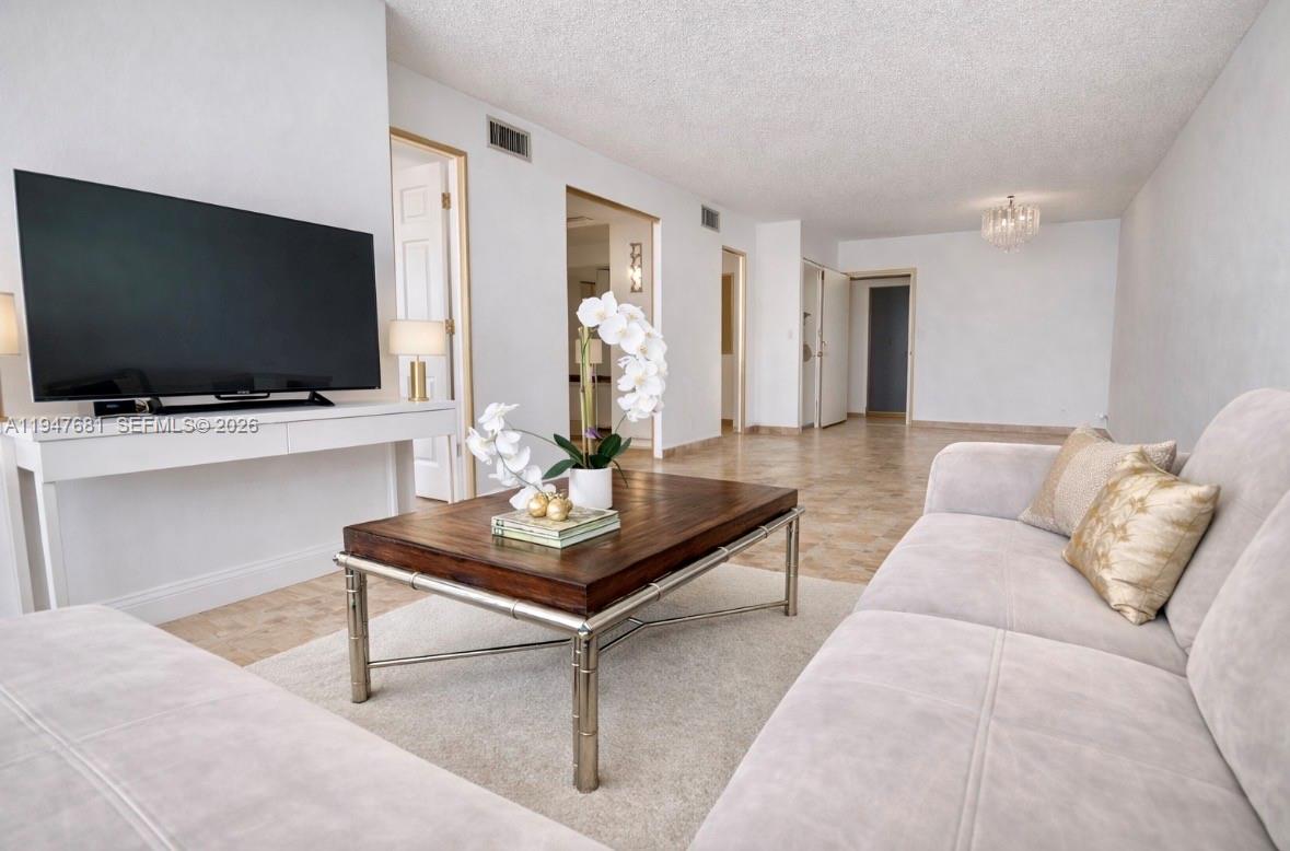 A living room features a large television, a wooden coffee table, and a light-colored sofa — 801 Three Islands Blvd # 411, Hallandale Beach FL 33009, HALLANDALE BEACH, FL