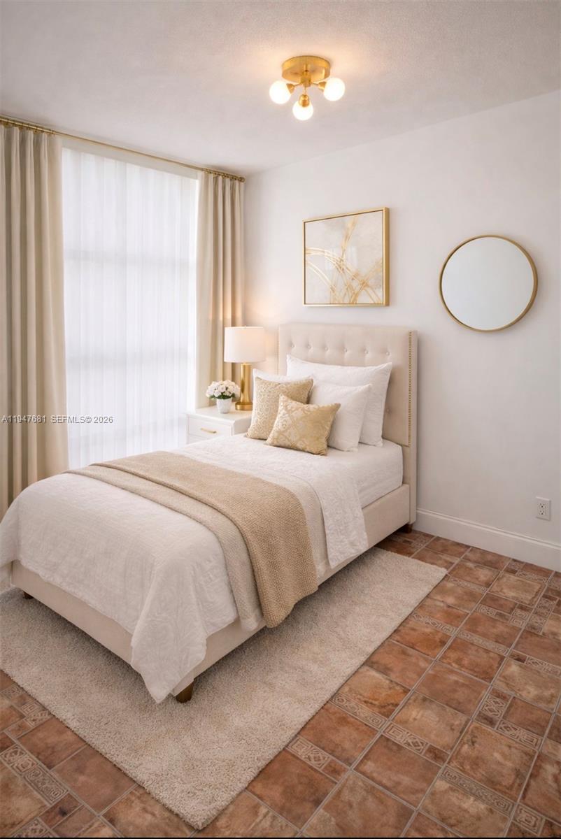 A bedroom features a twin bed, neutral decor, a gold light fixture, and tiled flooring — 801 Three Islands Blvd # 411, Hallandale Beach FL 33009, HALLANDALE BEACH, FL