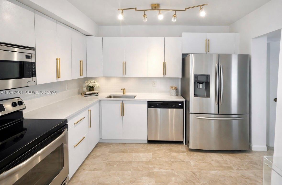 A kitchen features white cabinets, gold hardware, stainless steel appliances, and light-colored tile flooring — 801 Three Islands Blvd # 411, Hallandale Beach FL 33009, HALLANDALE BEACH, FL