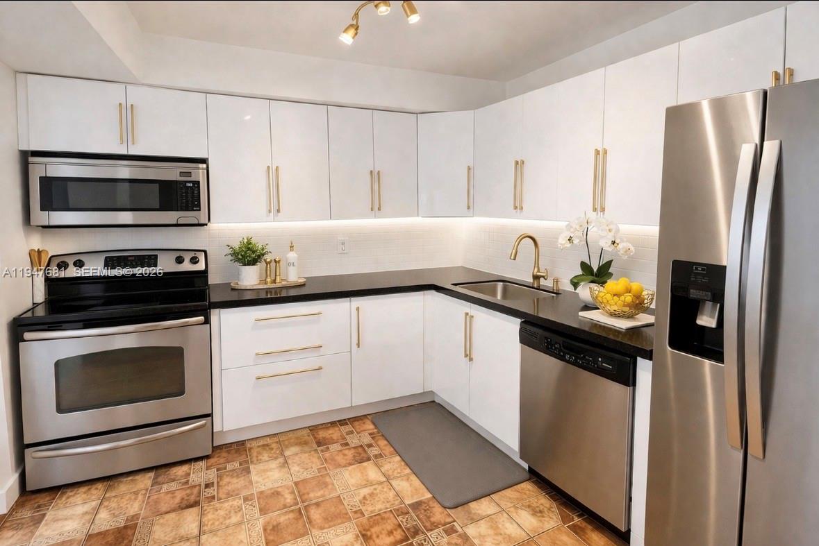 A kitchen with white cabinets, gold hardware, black countertops, and stainless steel appliances — 801 Three Islands Blvd # 411, Hallandale Beach FL 33009, HALLANDALE BEACH, FL