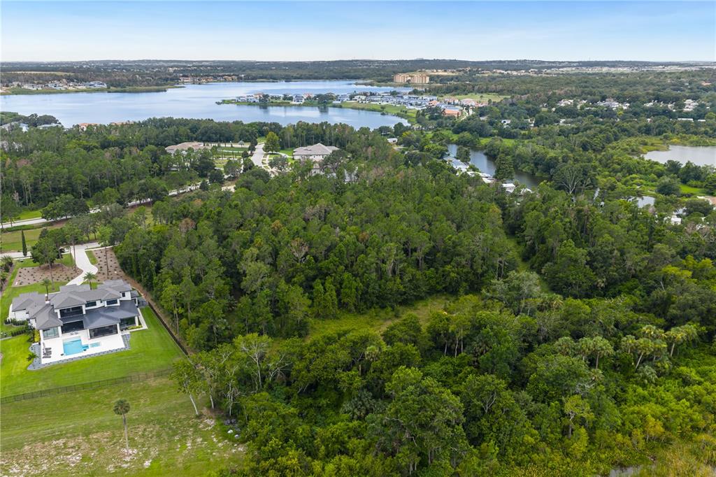 An aerial view shows a large wooded lot next to a modern house and lake — 17001 LUCCA LANE, BELLA COLLINA, FL