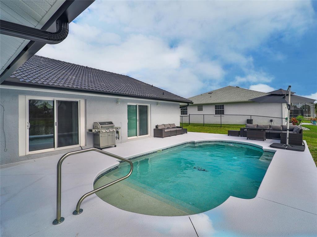 A backyard patio features a swimming pool, a grill, and outdoor seating furniture — 2 CEDAR COURT, PALM COAST, FL