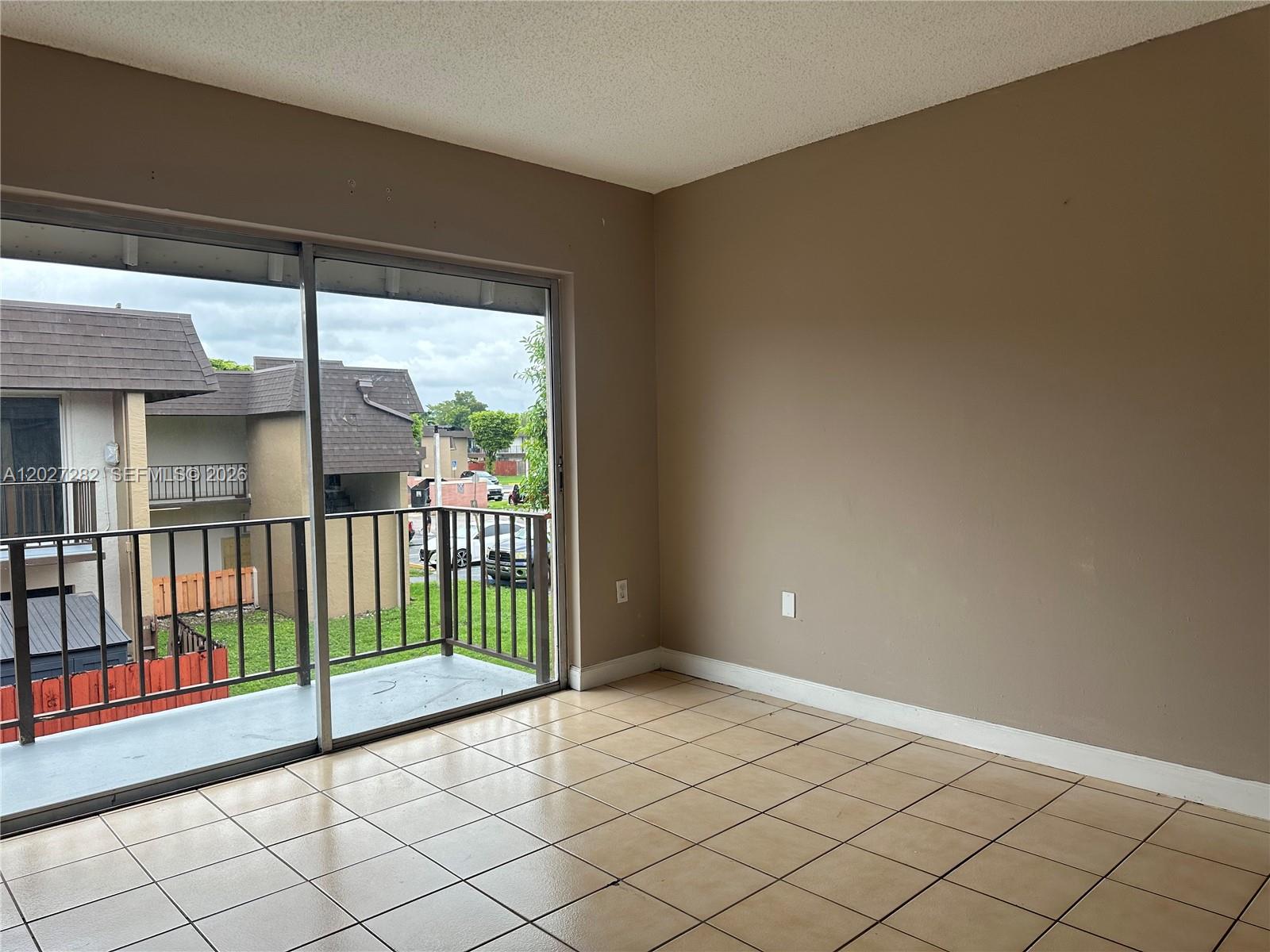 An empty room features beige tile flooring, tan walls, and a sliding glass door to a balcony — 890 SW 129th Pl # 208, Miami FL 33184, MIAMI, FL