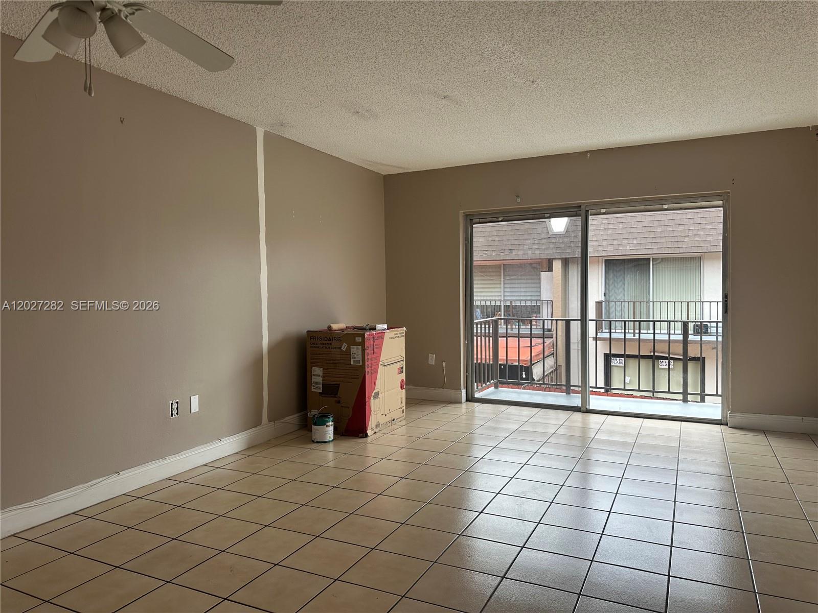 An empty room features beige walls, tiled floors, a ceiling fan, and a sliding glass door — 890 SW 129th Pl # 208, Miami FL 33184, MIAMI, FL