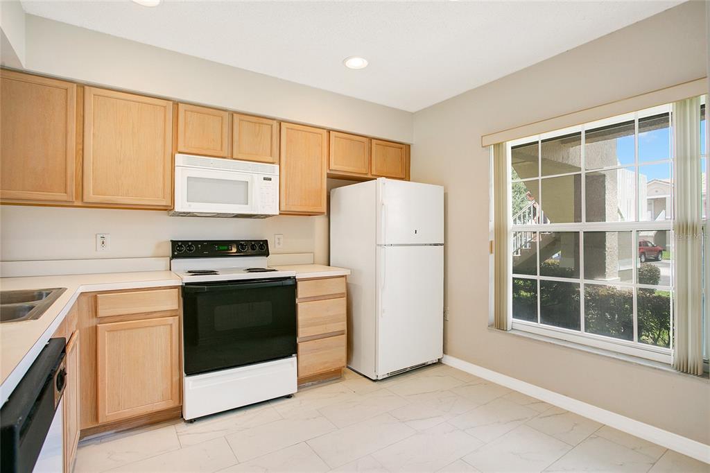 A kitchen with light wood cabinets, white appliances, and tile flooring next to a window — 13324 FAIRWAY GLEN DRIVE UNIT 101, ORLANDO, FL