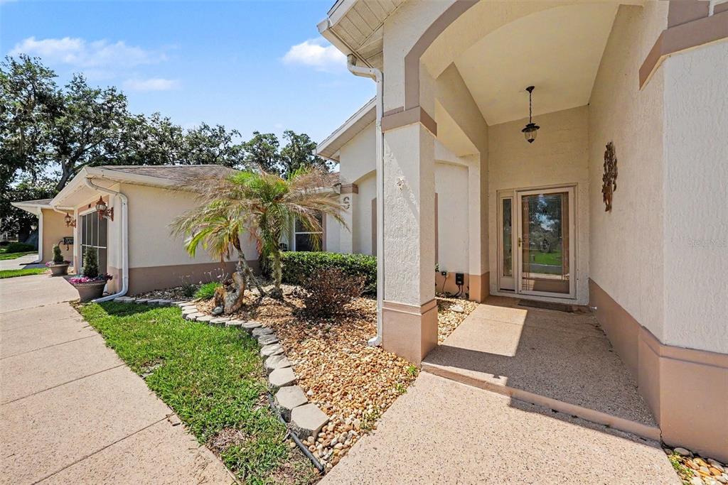 A beige stucco house exterior features a covered entryway, a palm tree, and gravel landscaping — 11132 MOSHIE LANE, SAN ANTONIO, FL