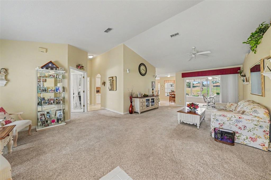 A living room with beige carpet, vaulted ceilings, a floral sofa, and a glass display cabinet — 11132 MOSHIE LANE, SAN ANTONIO, FL