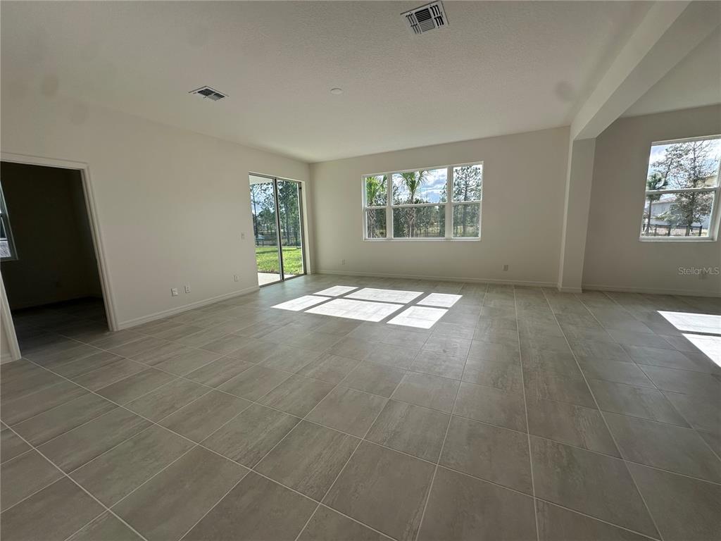 An empty living room features large windows, sliding glass doors, and light-colored tile flooring — 2000 BEEVALLEY WAY, DELAND, FL