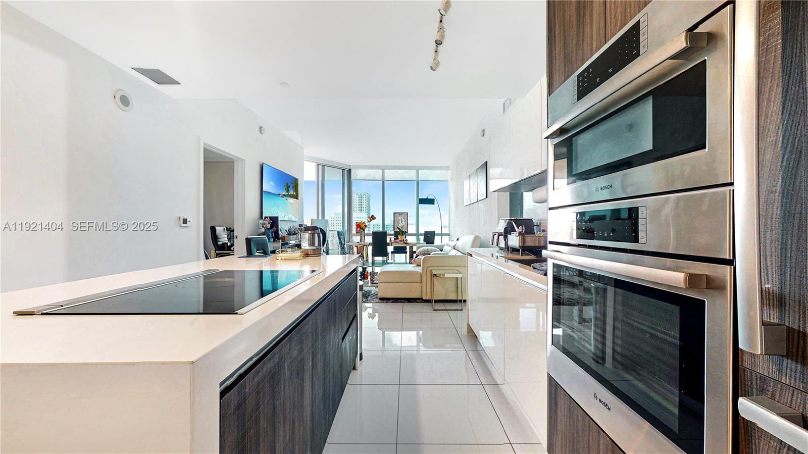 A modern kitchen with a central island and stainless steel appliances opens into a living area — 851 NE 1st Ave # 1508, Miami FL 33132, MIAMI, FL