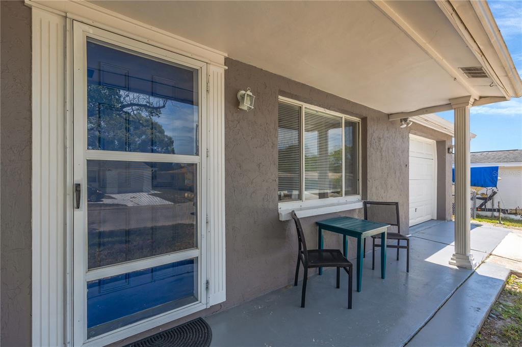 A covered front porch features a storm door, a window, and a small patio table set — 7804 NIAGARA DRIVE, PORT RICHEY, FL
