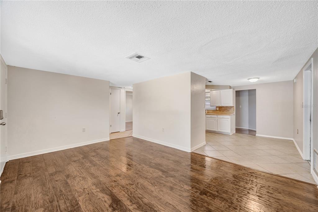 A room with dark wood flooring transitions into a tiled kitchen area with white cabinets — 7804 NIAGARA DRIVE, PORT RICHEY, FL