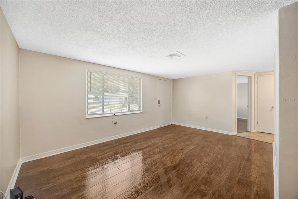 An empty room with light-colored walls, wood-look flooring, a window with blinds, and two doors — 7804 NIAGARA DRIVE, PORT RICHEY, FL
