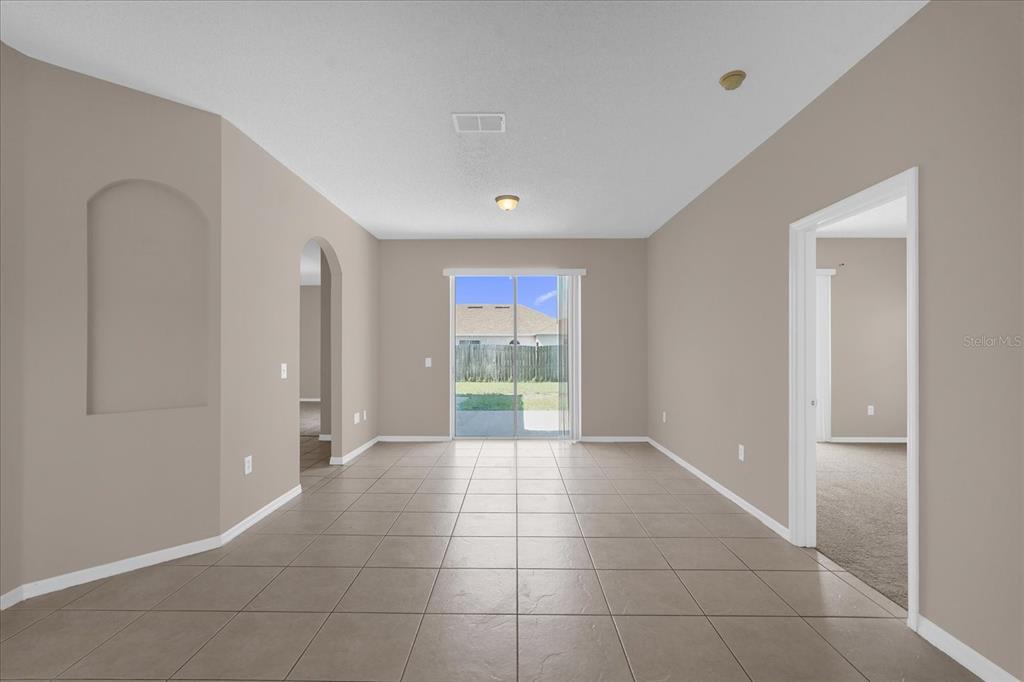 An empty room with beige walls, tile flooring, and a sliding glass door to the backyard — 29 ANDORA COURT, KISSIMMEE, FL