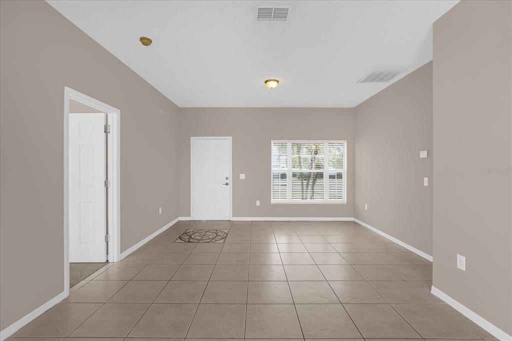 An empty room with beige walls, tile flooring, a white door, and a window — 29 ANDORA COURT, KISSIMMEE, FL