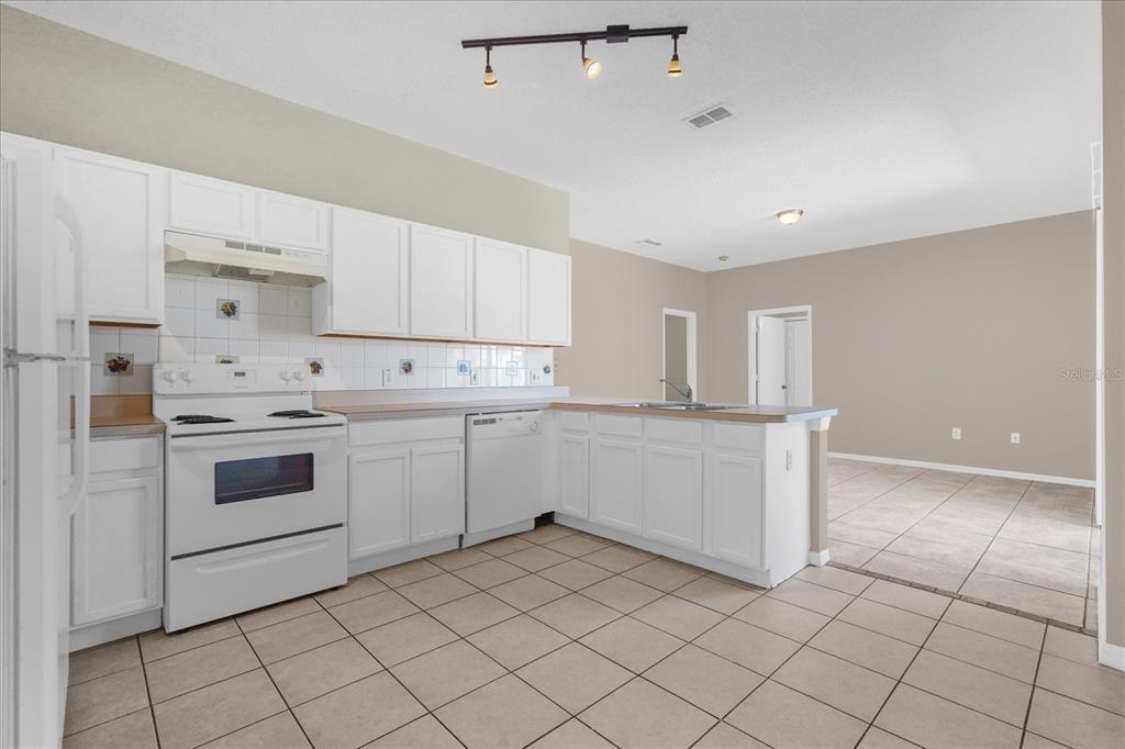 A kitchen with white cabinets, white appliances, and tiled flooring opens into a living area — 29 ANDORA COURT, KISSIMMEE, FL