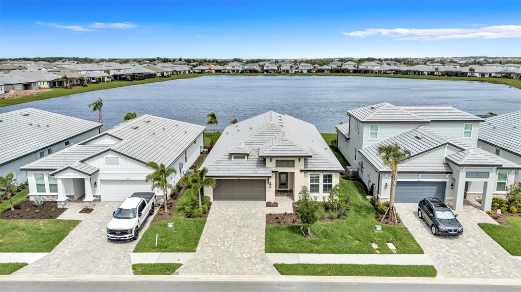 An aerial view shows three suburban houses with tiled roofs situated along a large lake — 17241 SAVORY MIST CIRCLE, BRADENTON, FL