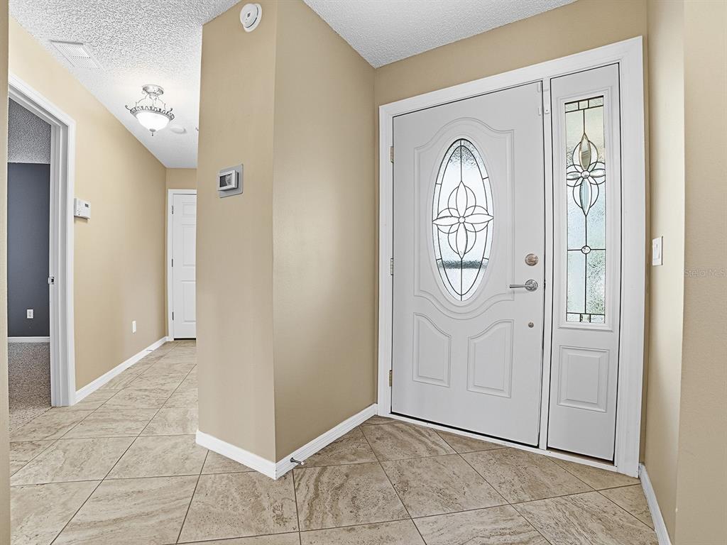 An entryway features tan tile flooring, beige walls, and a white front door with glass — 579 CHERAW PLACE, THE VILLAGES, FL