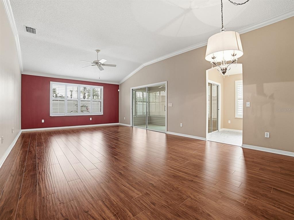 A living room with wood-look flooring, a red accent wall, and a ceiling fan — 579 CHERAW PLACE, THE VILLAGES, FL