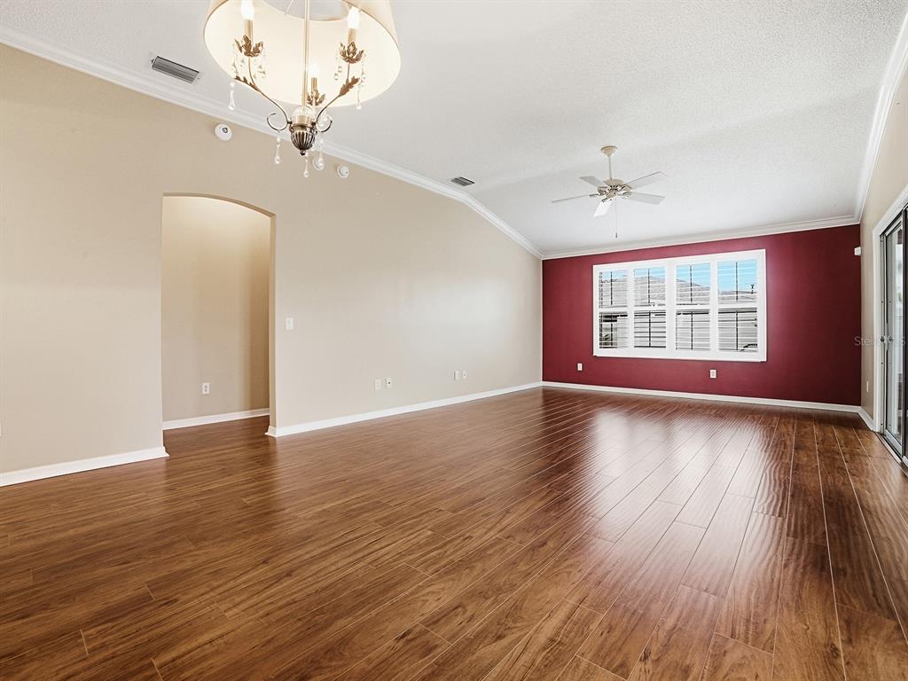 A spacious living room features wood-look flooring, a vaulted ceiling, and a red accent wall — 579 CHERAW PLACE, THE VILLAGES, FL