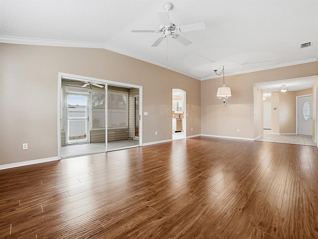 A spacious living room features wood-look flooring, a ceiling fan, and sliding glass patio doors — 579 CHERAW PLACE, THE VILLAGES, FL