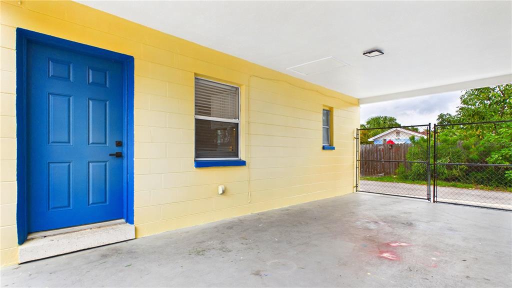 A covered concrete patio features a bright blue door and yellow concrete block walls — 3815 1ST AVE N UNIT C, ST PETERSBURG, FL
