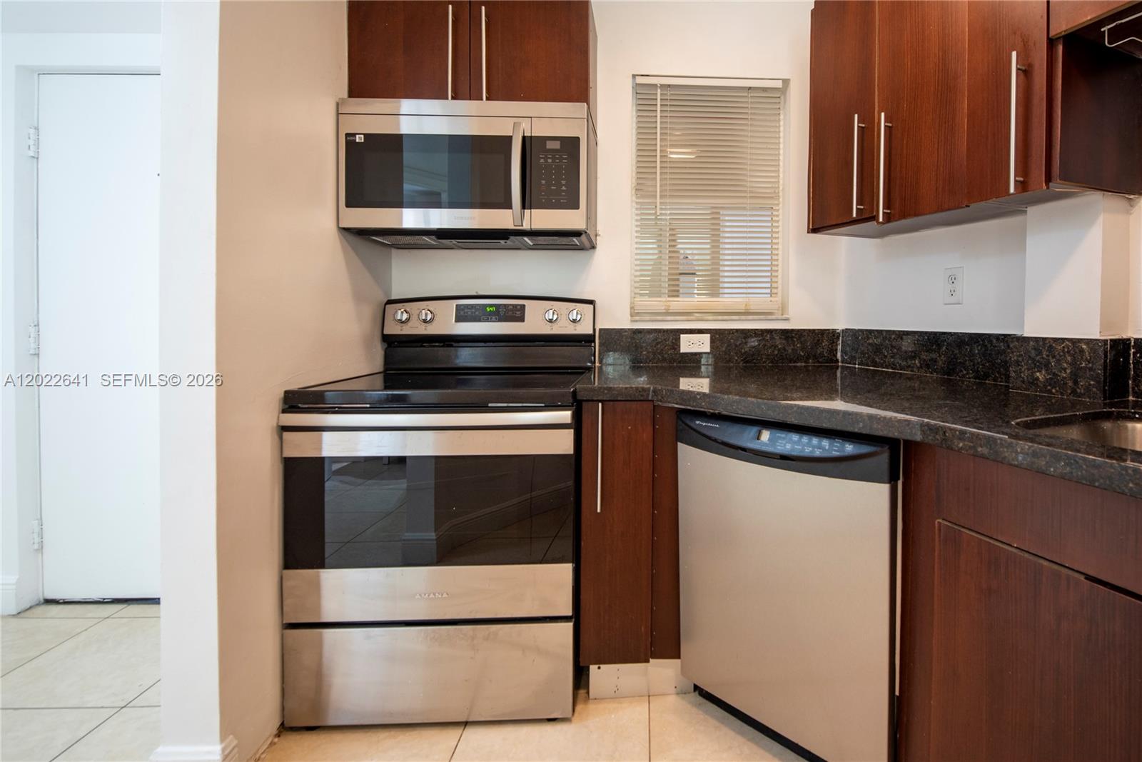 A kitchen features stainless steel appliances, dark wood cabinetry, and black granite countertops — 4147 Stirling Rd # 105, Dania Beach FL 33314, DANIA BEACH, FL