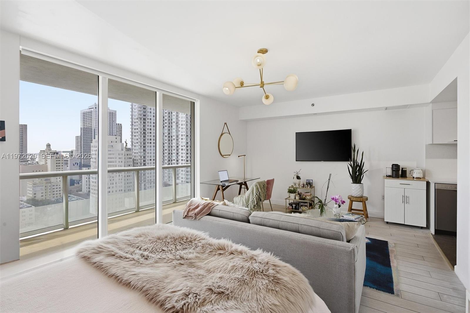 A modern studio apartment features a sofa, desk, kitchenette, and a balcony with city views — 50 Biscayne Blvd # 1909, Miami FL 33132, MIAMI, FL