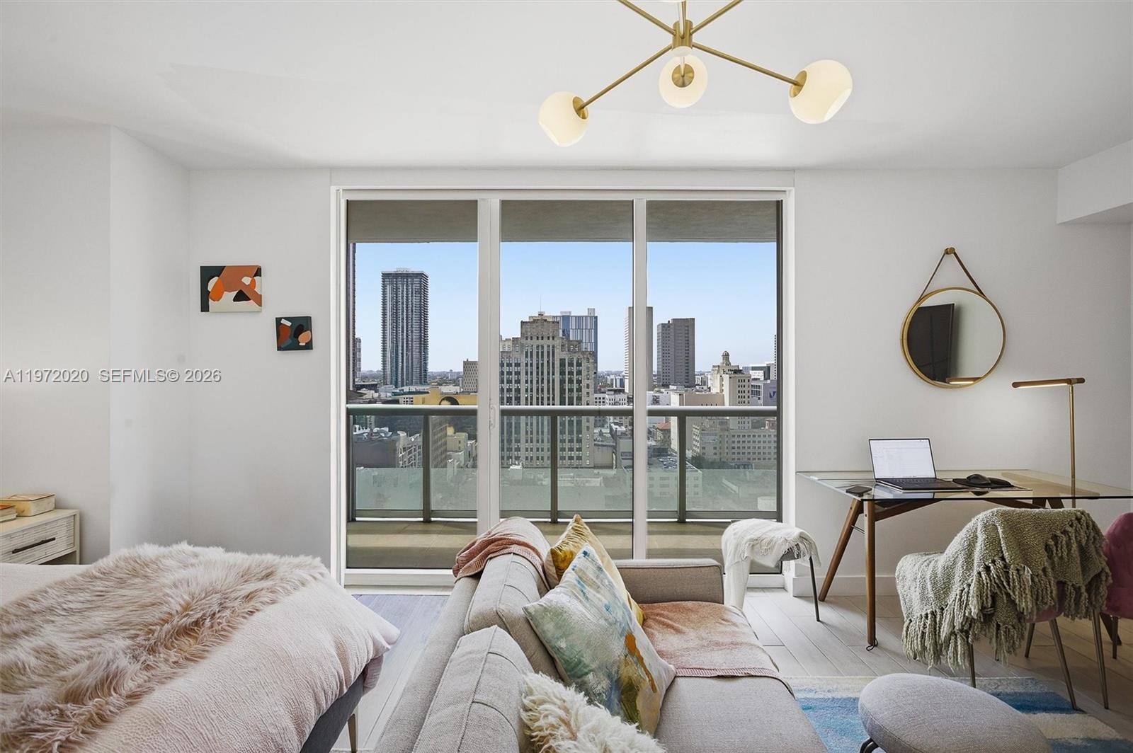 A modern bedroom features a sofa, a desk, and a balcony overlooking a city skyline — 50 Biscayne Blvd # 1909, Miami FL 33132, MIAMI, FL