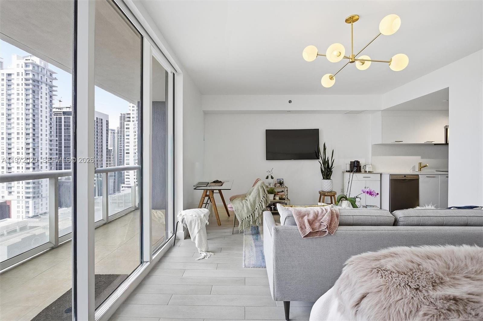 A modern living room with a grey sofa, white tile floors, and a balcony view — 50 Biscayne Blvd # 1909, Miami FL 33132, MIAMI, FL