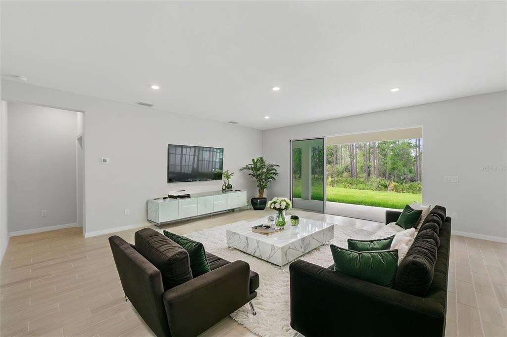 A modern living room features a white marble coffee table, dark sofas, and large sliding doors — 1645 TRAILHEAD LANE, ZEPHYRHILLS, FL