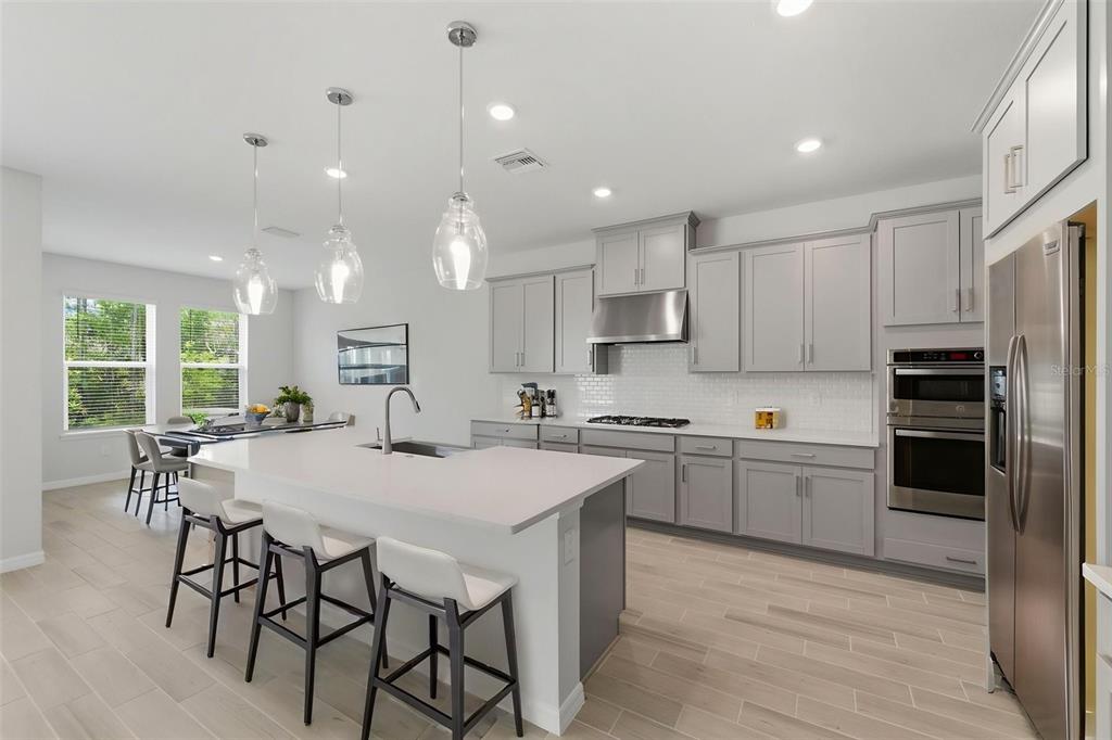 A modern kitchen features gray cabinets, white countertops, a central island, and stainless steel appliances — 1645 TRAILHEAD LANE, ZEPHYRHILLS, FL