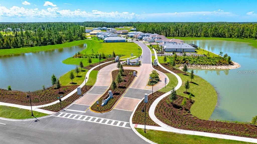 An aerial view shows a gated community entrance with a divided road between two ponds — 1645 TRAILHEAD LANE, ZEPHYRHILLS, FL