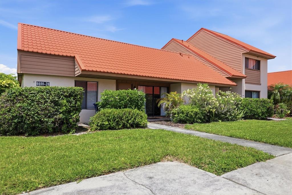 A single-story residential building features a prominent orange tiled roof and tan siding — 6628 DRAW LANE UNIT 122, SARASOTA, FL