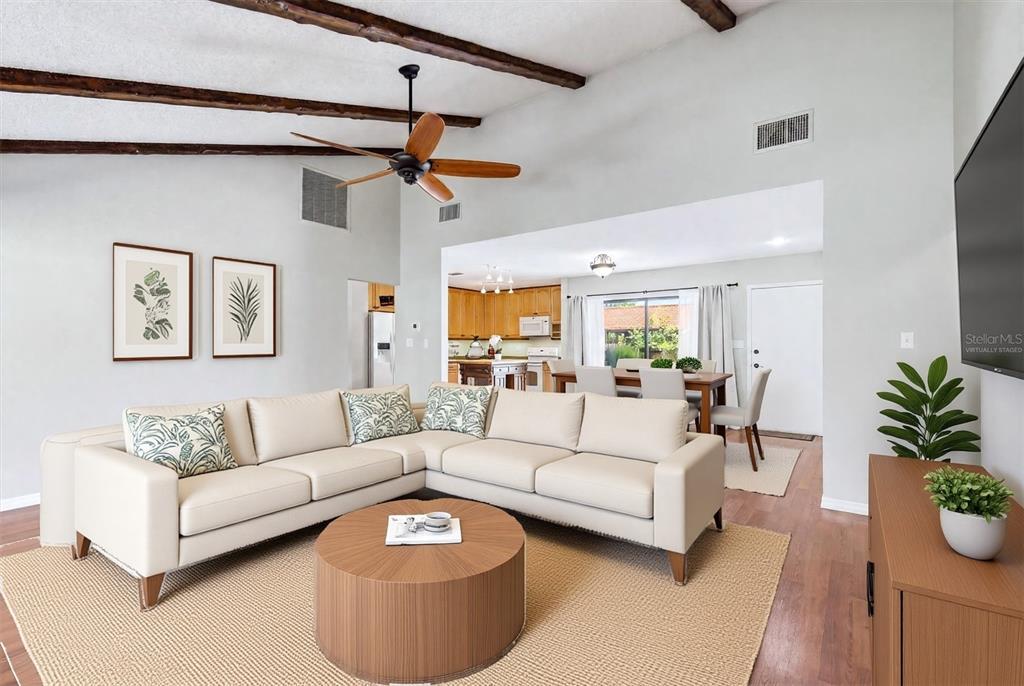A living room with a sectional sofa, wooden ceiling beams, and an open kitchen view — 6628 DRAW LANE UNIT 122, SARASOTA, FL