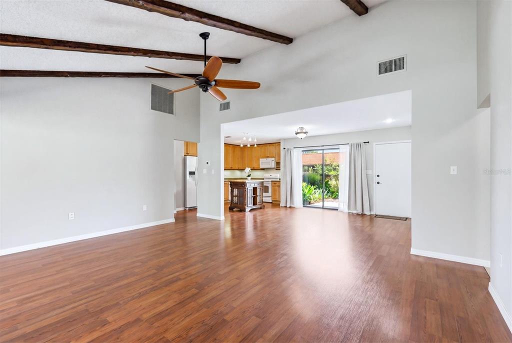 An open-concept living area with wood-look flooring, vaulted ceilings with exposed beams, and a kitchen — 6628 DRAW LANE UNIT 122, SARASOTA, FL